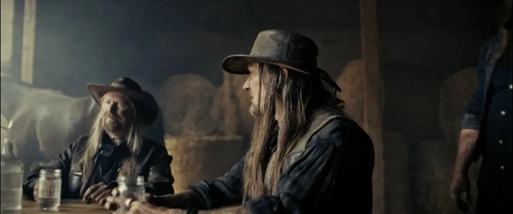 Two bearded, long-haired men in hats sitting at a table with mason jars in a smoky barn - Amon Amarth