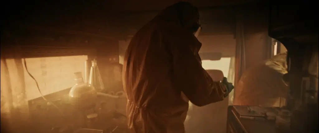 Figure in a hooded protective suit and gas mask inside a hazy, amber-lit caravan - Amon Amarth