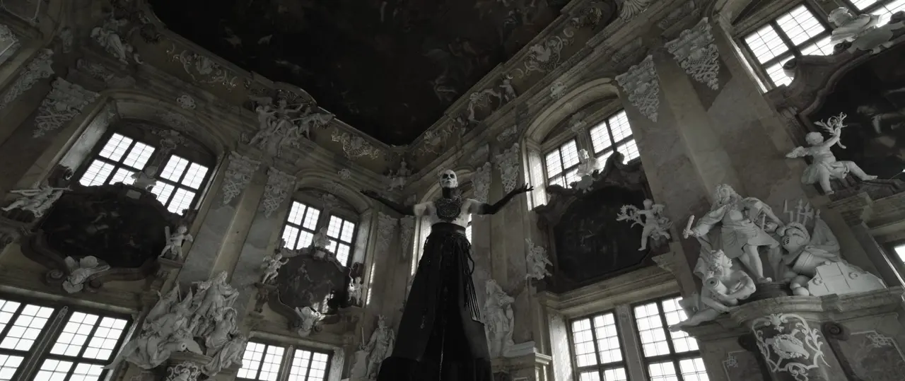 Behemoth music video still - low angle in a baroque hall, figure with arms raised