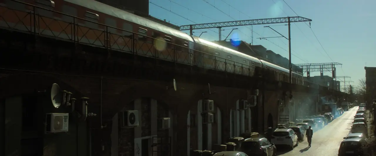 Passenger train crossing a brick viaduct above a sunlit street