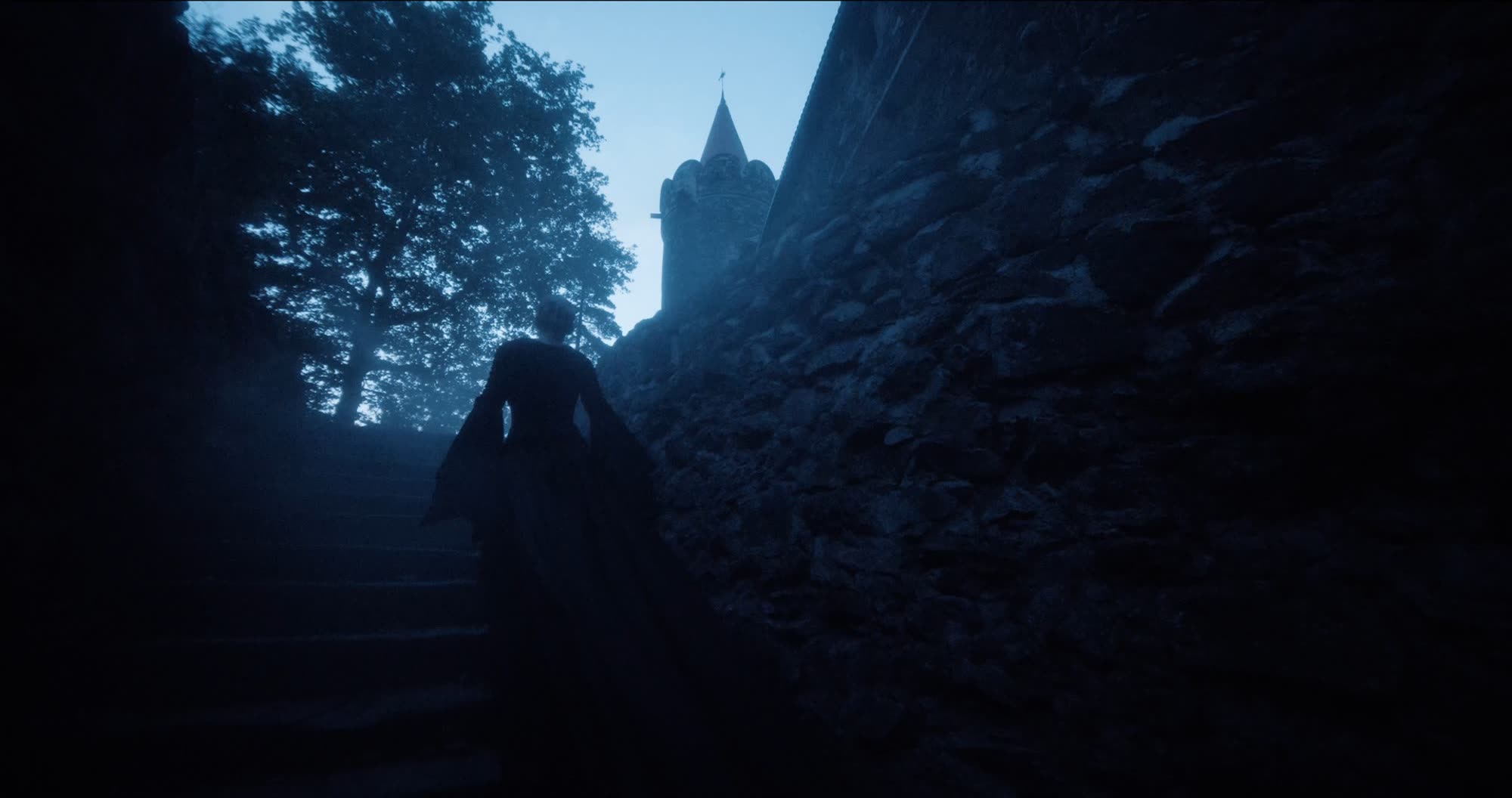 Ater music video still - figure in a dark gown ascending stone steps toward a castle tower at dusk