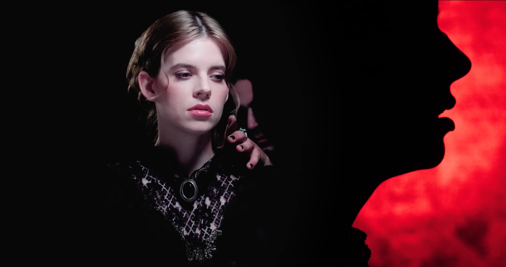 Ater music video still - close portrait in red and black light, hand raised to the chin