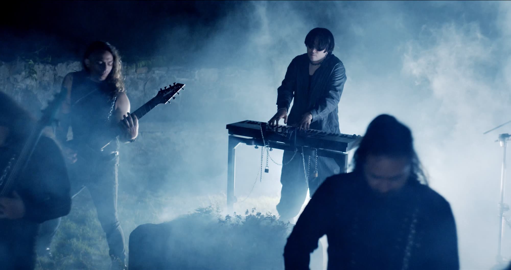 Ater music video still - keyboardist performing in blue fog beside a stone wall