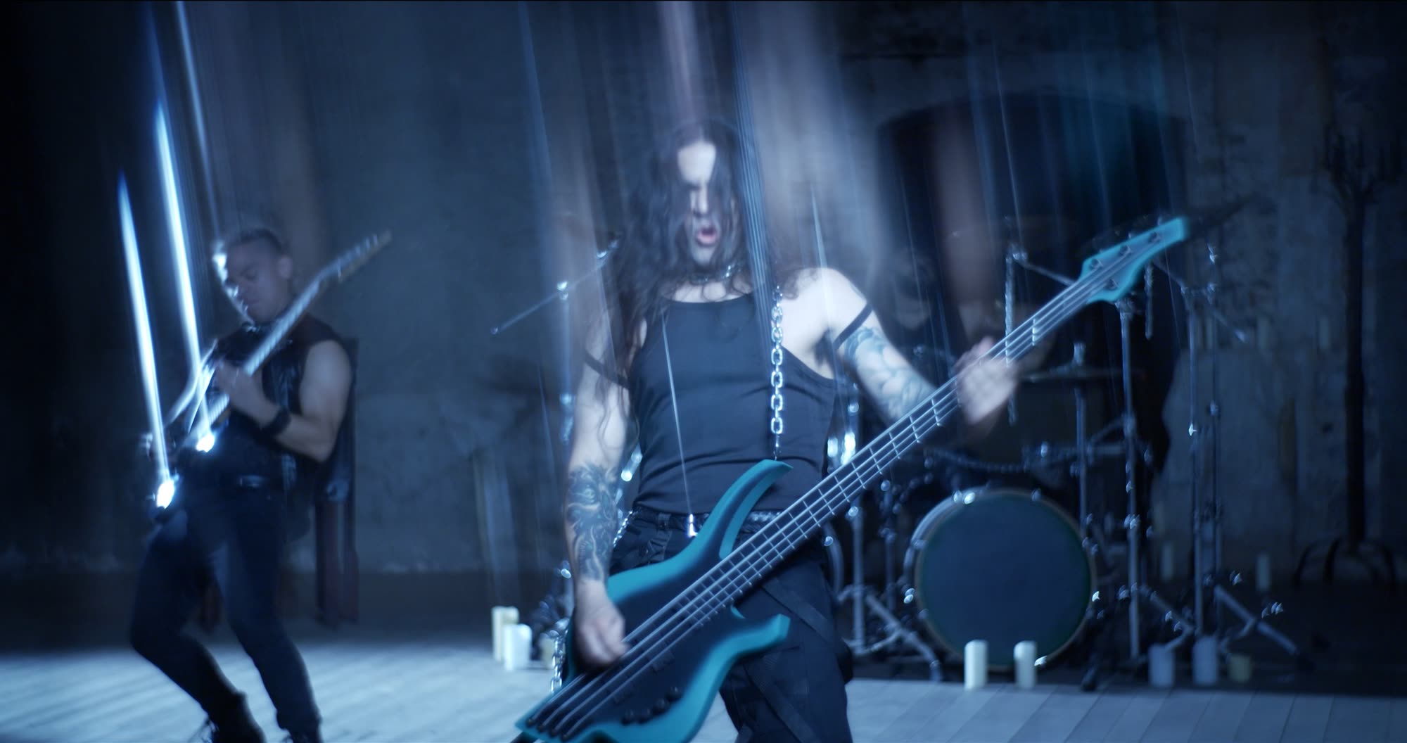 Ater music video still - tattooed bassist performing under streaked blue light beside another guitarist