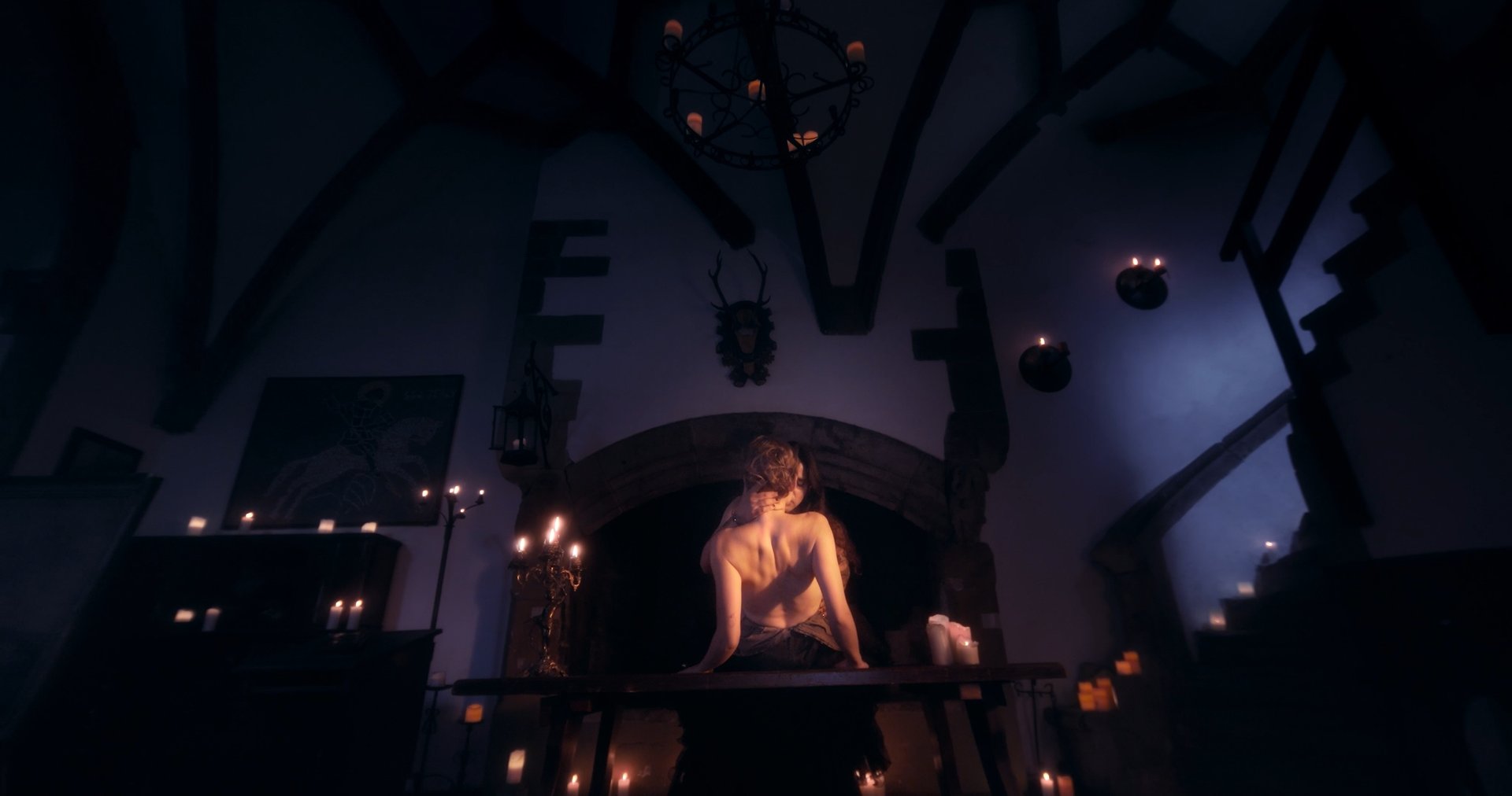 Ater music video still - intimate candlelit moment by a stone fireplace, two figures embracing