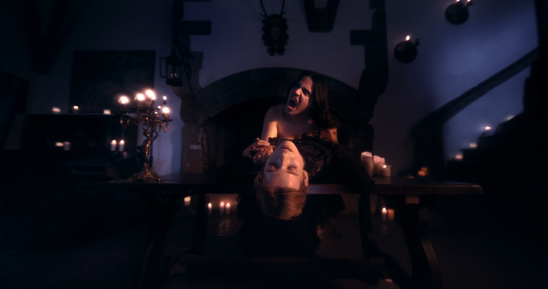 Ater music video still - two figures reclined at a candlelit table in a vampiric embrace