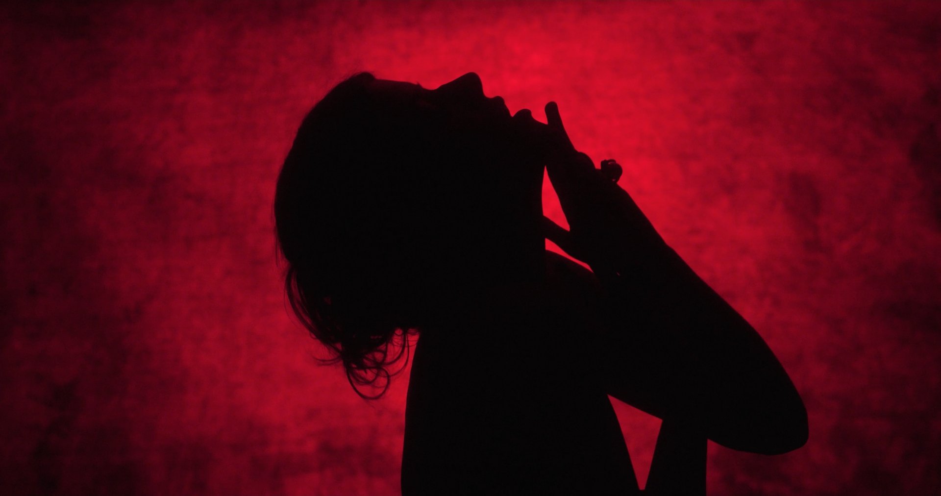 Ater music video still - red-lit silhouette singing, hand raised to the face