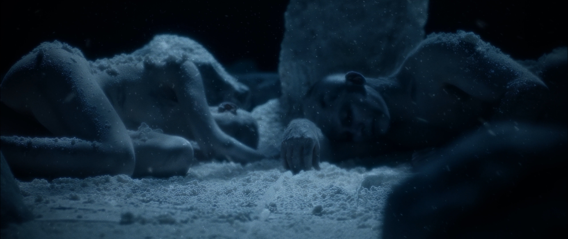 Behemoth Mystic still - a frost-covered figure lying in the snow, eyes open, hand reaching forward