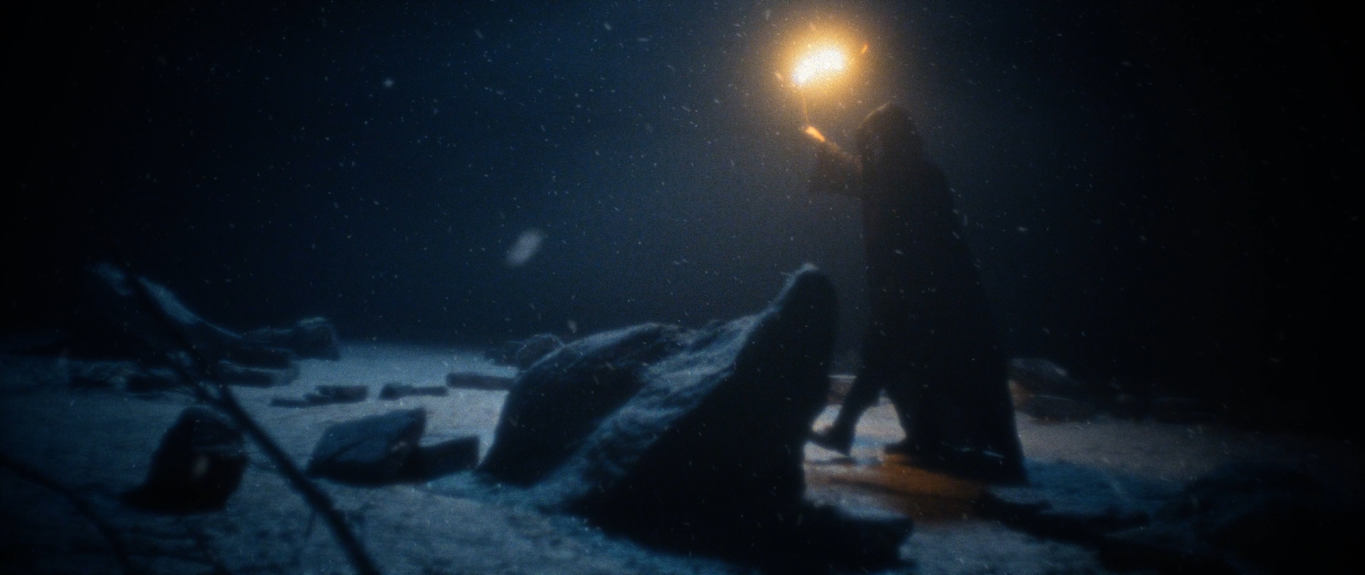 Behemoth Mystic still - cloaked figure carrying a torch past snow-covered standing stones
