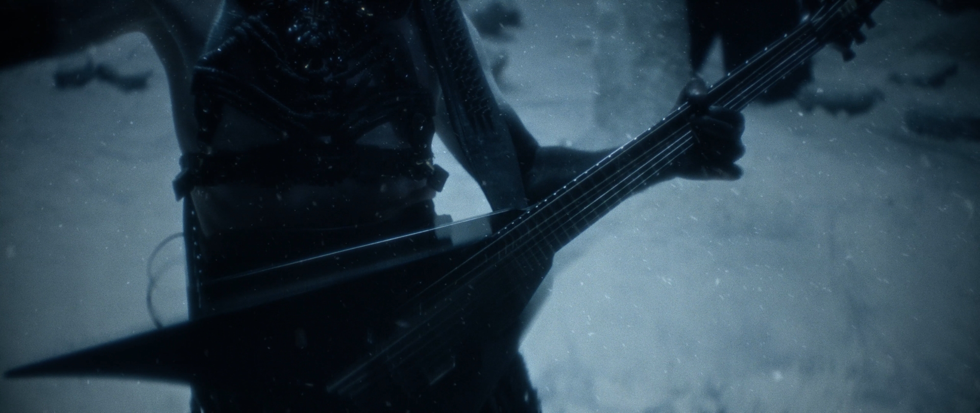 Behemoth Mystic still - close-up of a spiked guitar body and belt against a snowy backdrop