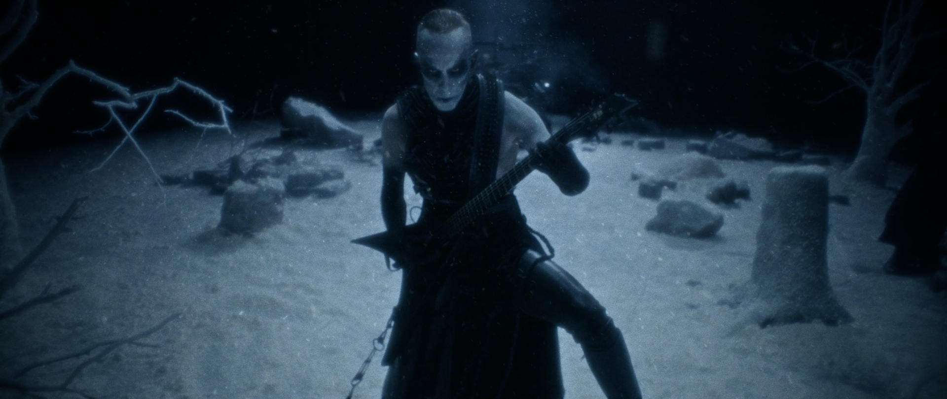 Behemoth Mystic still - corpsepainted guitarist standing among standing stones and bare trees in blue mist