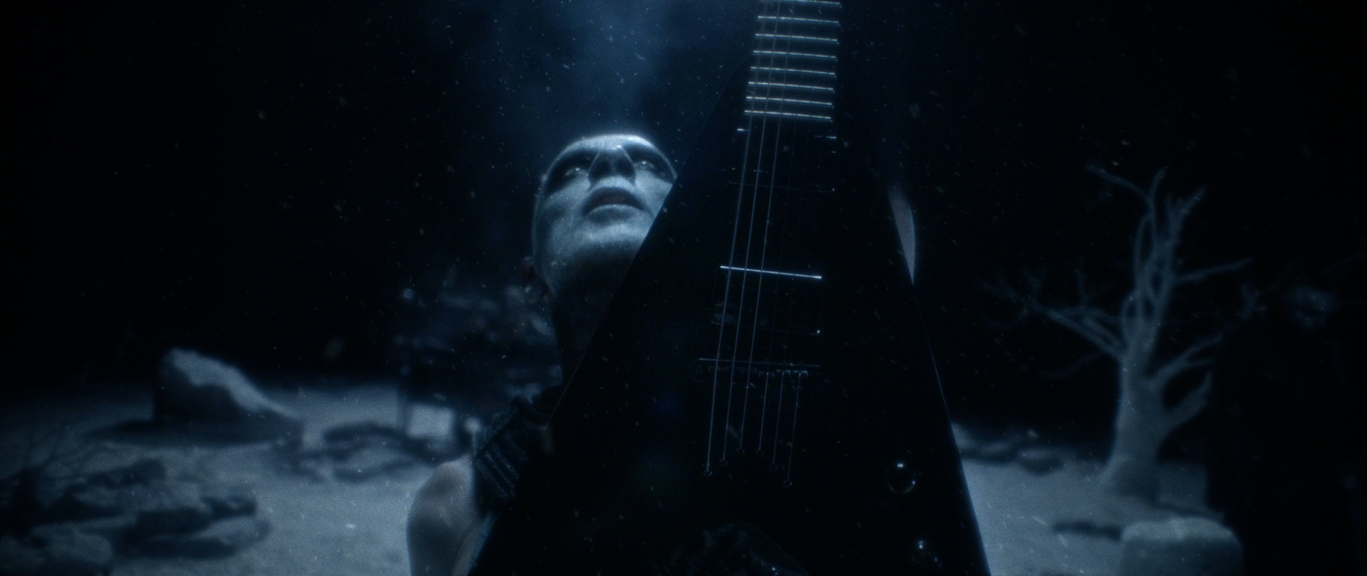 Behemoth Mystic still - corpsepainted guitarist looking upward past the guitar neck amid rocks and bare trees
