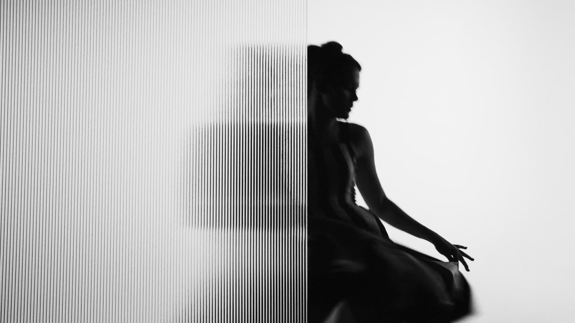 Dzień i noc still - model in profile seen through reeded glass, bright white studio beyond