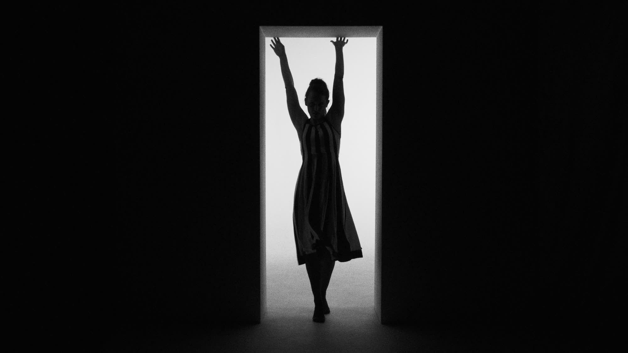 Dzień i noc still - silhouette in a striped dress, arms raised inside a narrow doorway of light