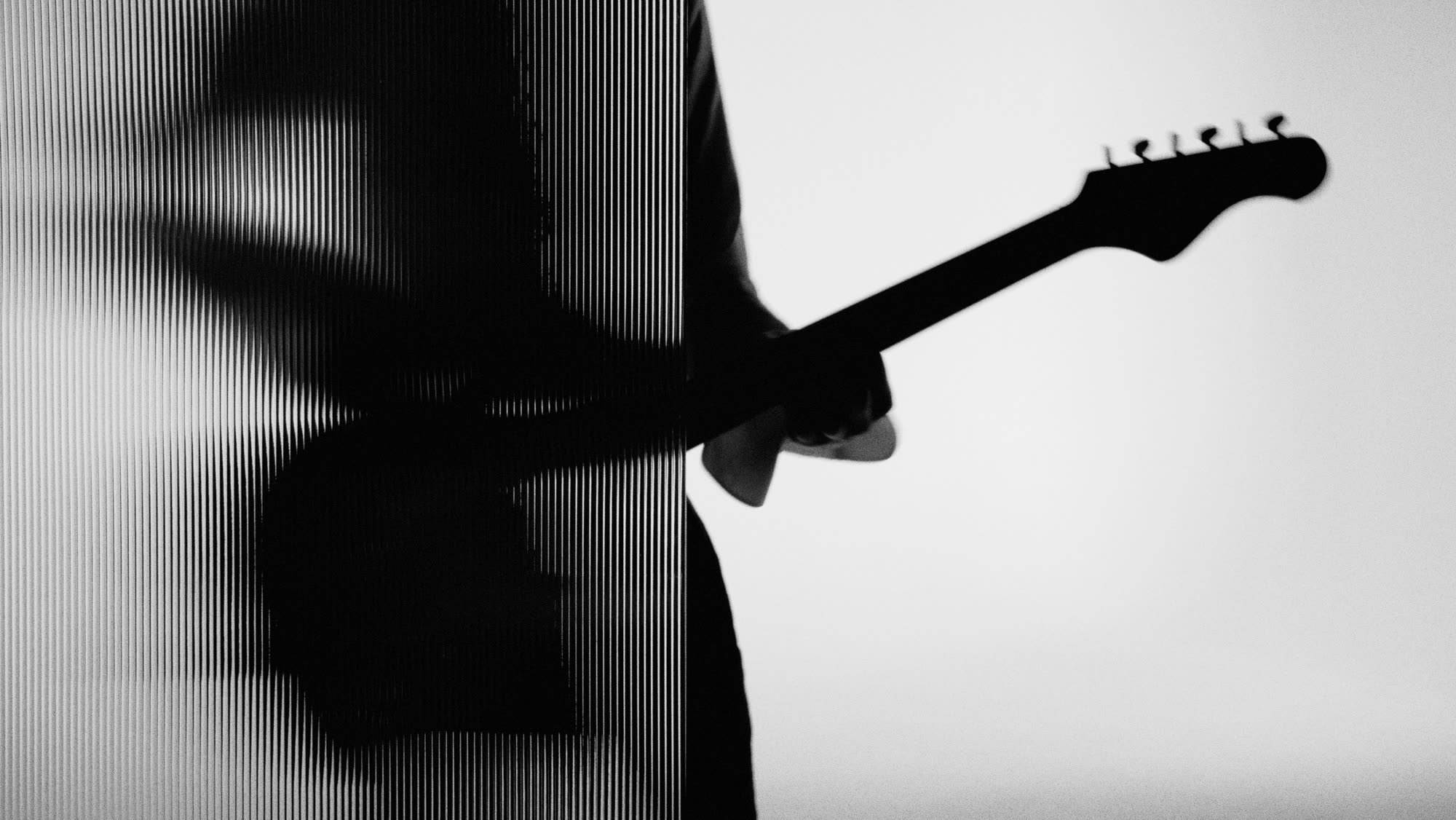 Dzień i noc still - guitar headstock in silhouette seen through a panel of reeded glass
