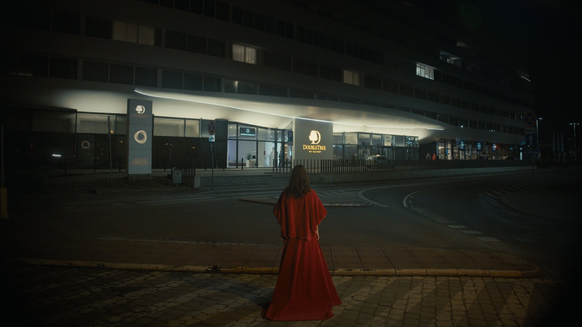Woman in a red cloak walking through a dark exterior at night - Wrocław Fashion Week 2025