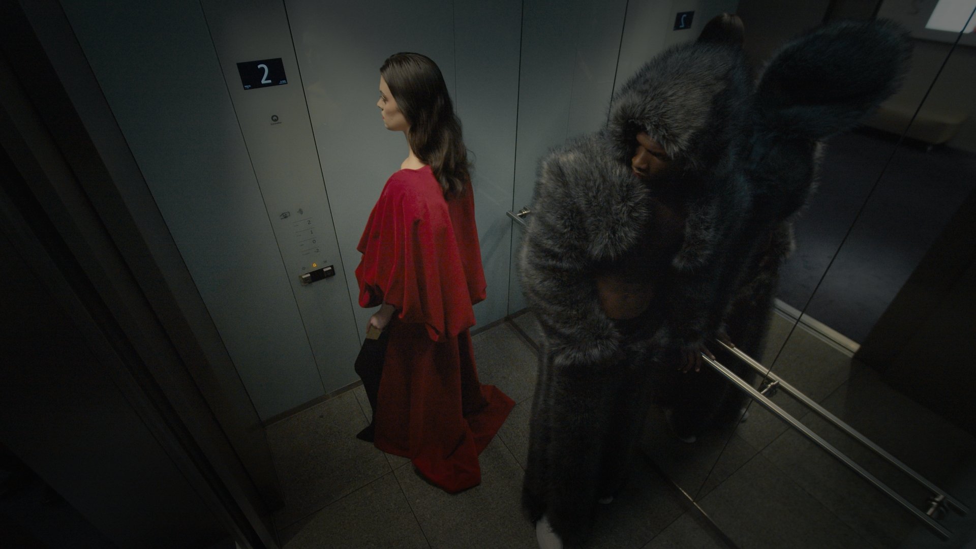 Woman in red beside a masked creature figure in a corridor - Wrocław Fashion Week 2025