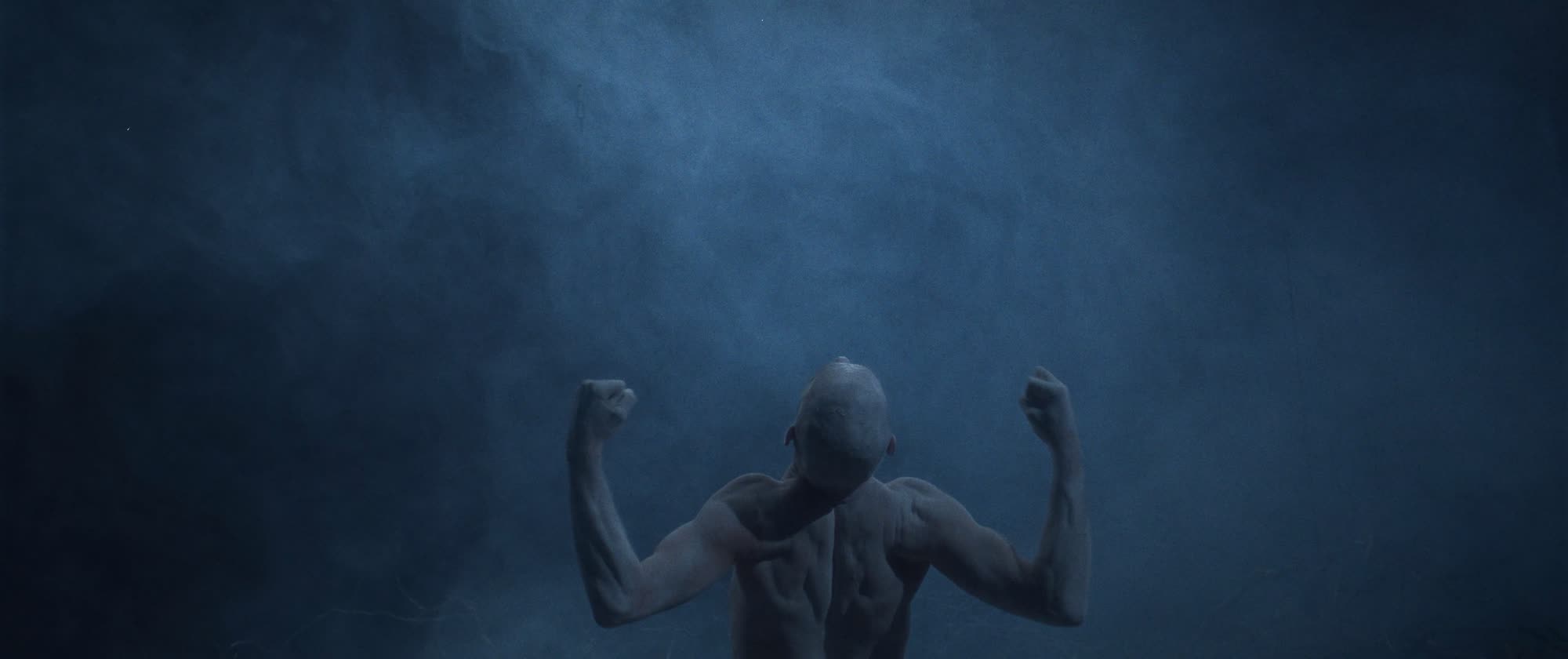 IGORRR music video still - muscular figure seen from behind, arms raised in blue fog