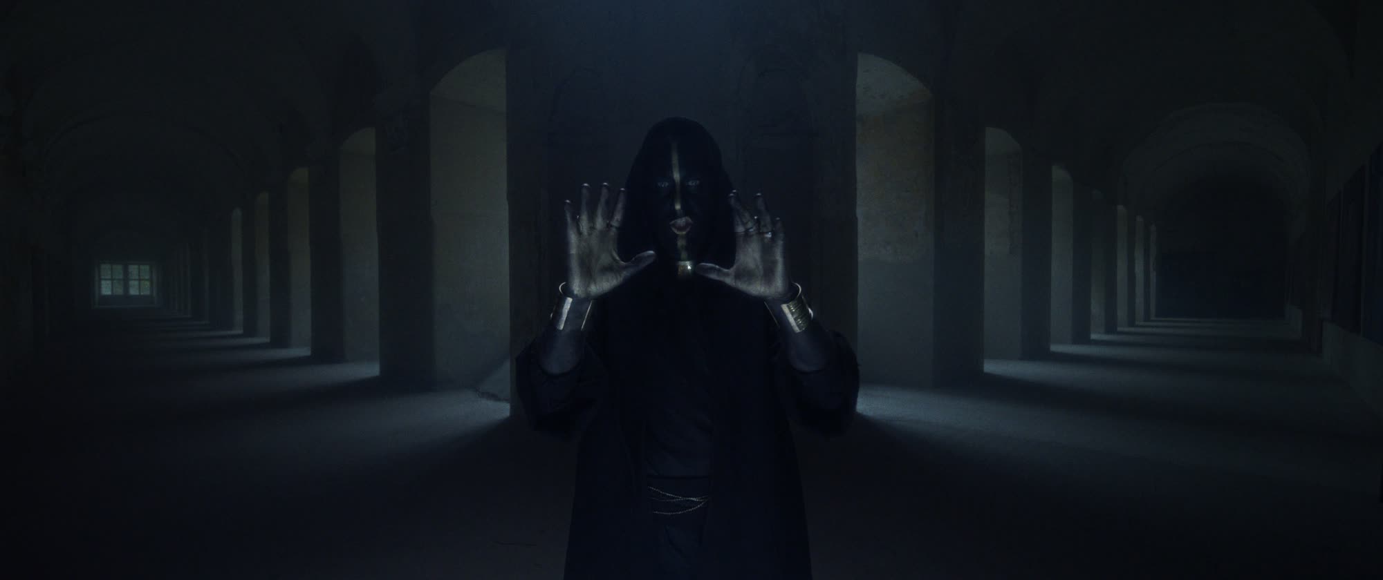 IGORRR music video still - hooded figure with painted face, palms raised toward the camera