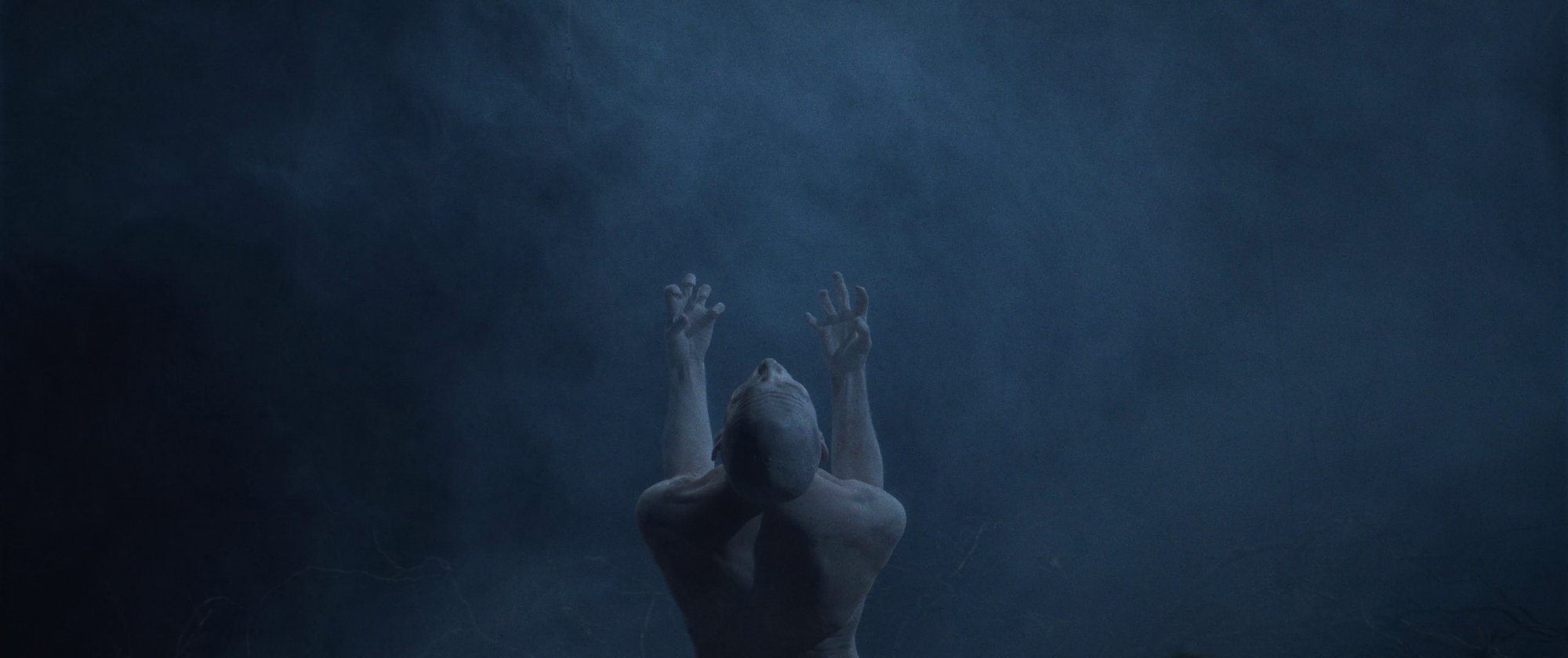 IGORRR music video still - pale figure with arms raised and clawed hands, head bowed in fog