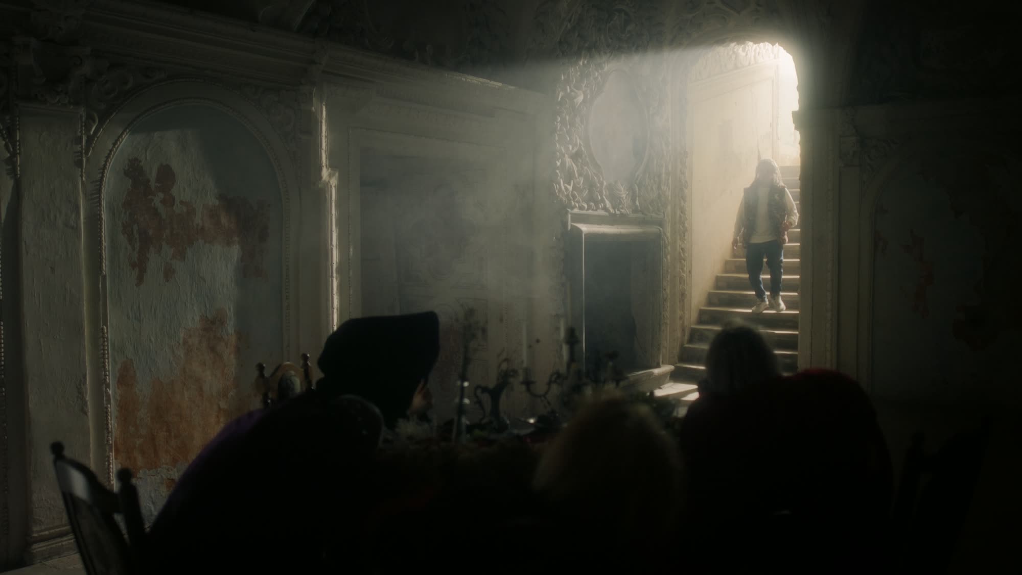 Jestem Alpha still - figure descending a grand staircase toward a bright doorway, blurred silhouettes in the foreground
