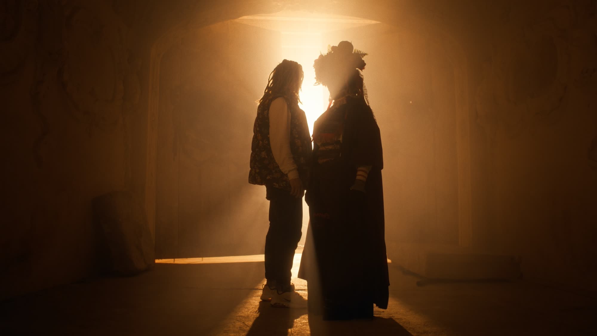 Jestem Alpha still - two silhouettes facing each other in a golden doorway, one in a floral folk headdress