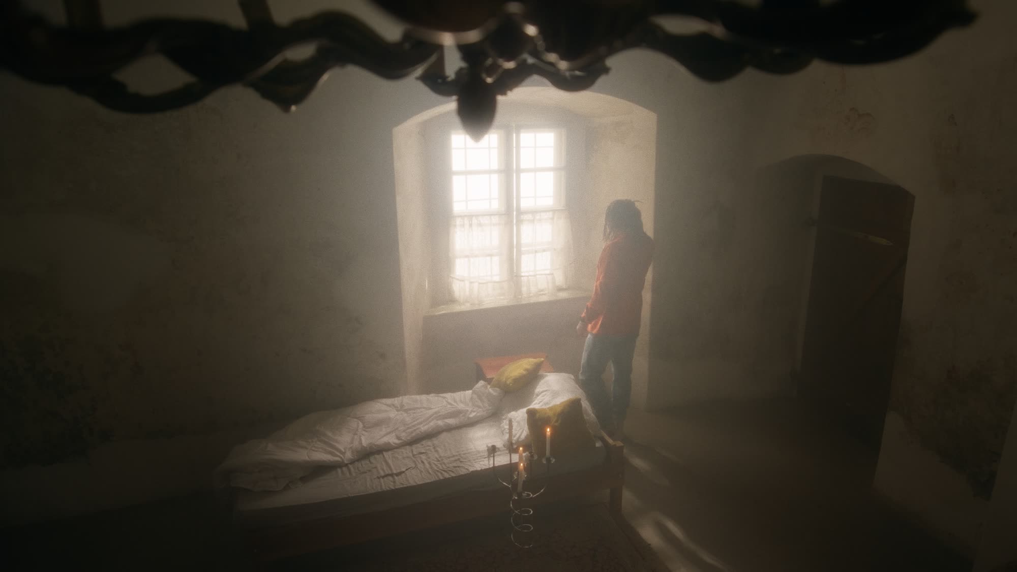 Jestem Alpha still - figure standing at a candlelit window beside an unmade bed