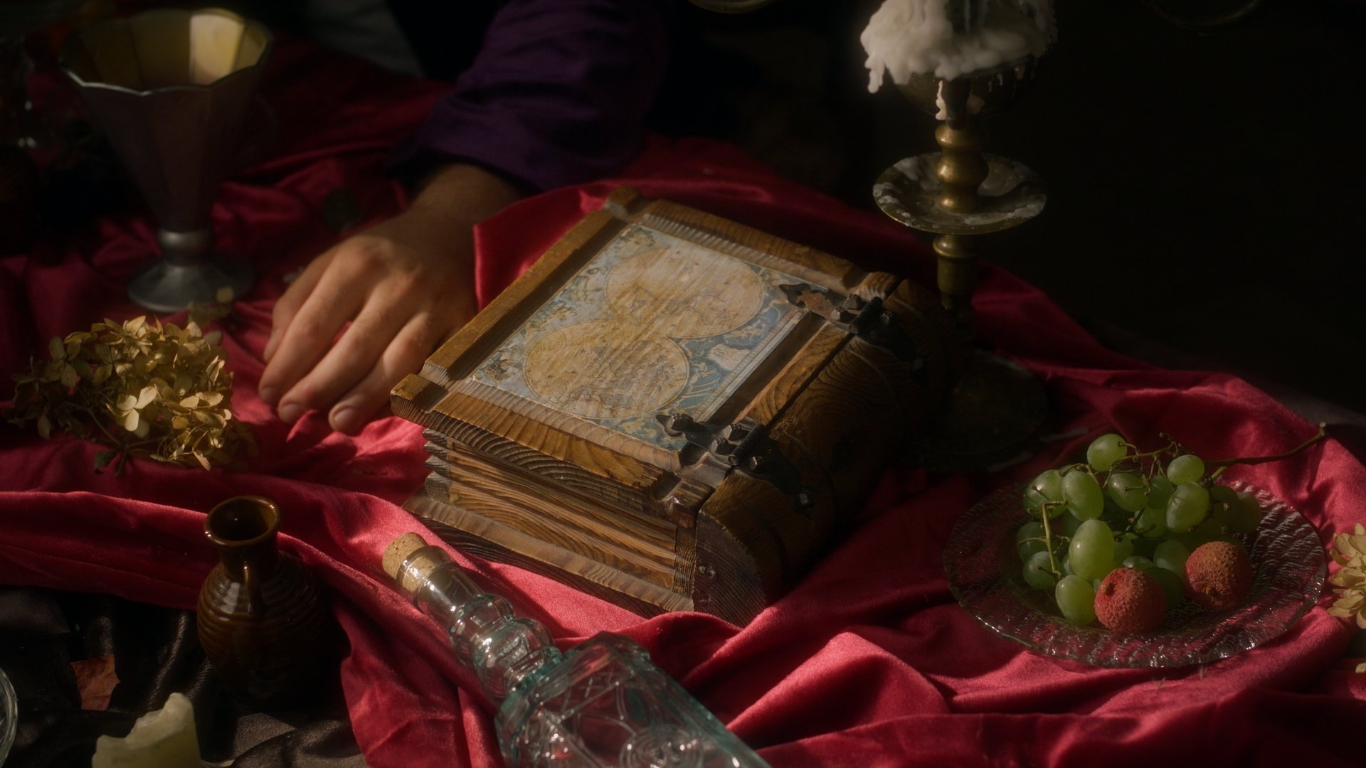 Jestem Alpha still - close-up of hands with an ornate book and jewelry on red fabric