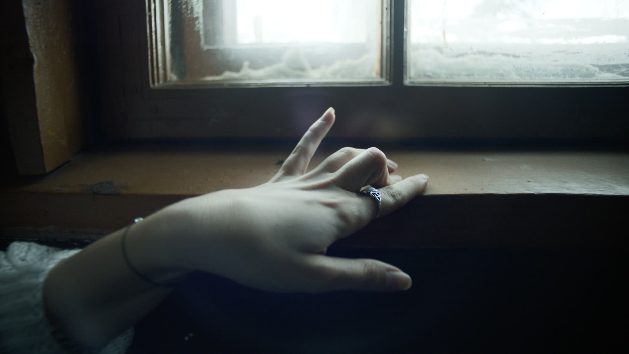 Close-up of a hand reaching toward a frost-covered windowsill