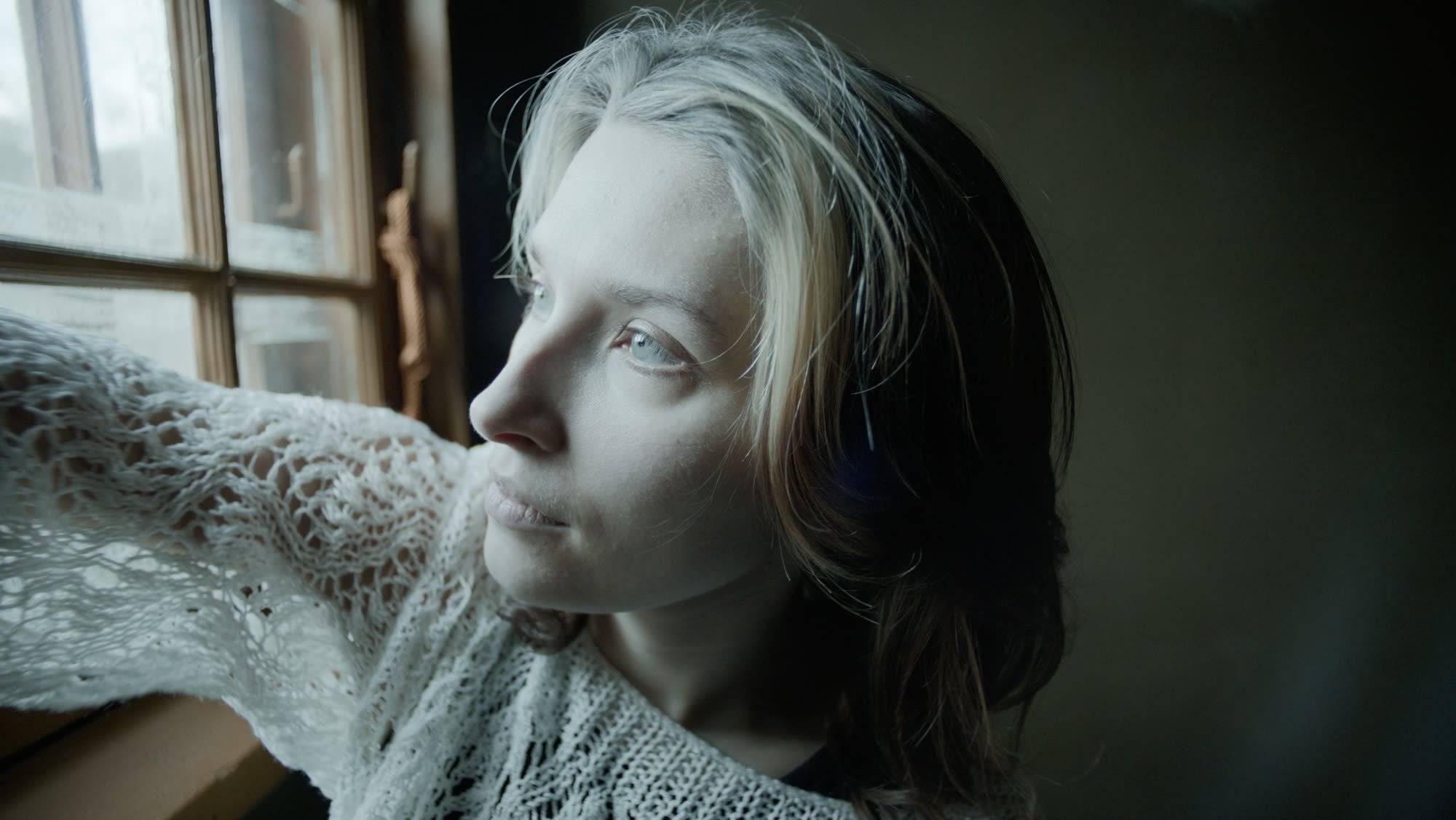 Close portrait looking out through a frosted window, cool daylight on her face