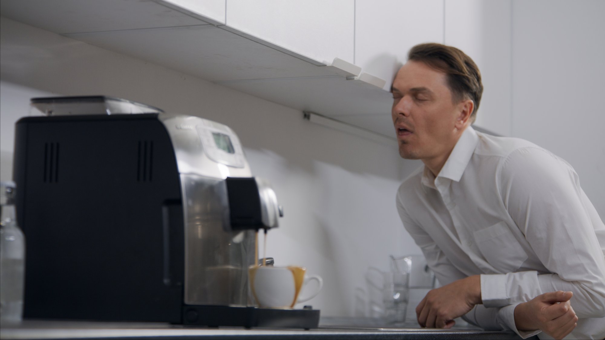 Man yawning dramatically beside an office espresso machine - Plantpur commercial
