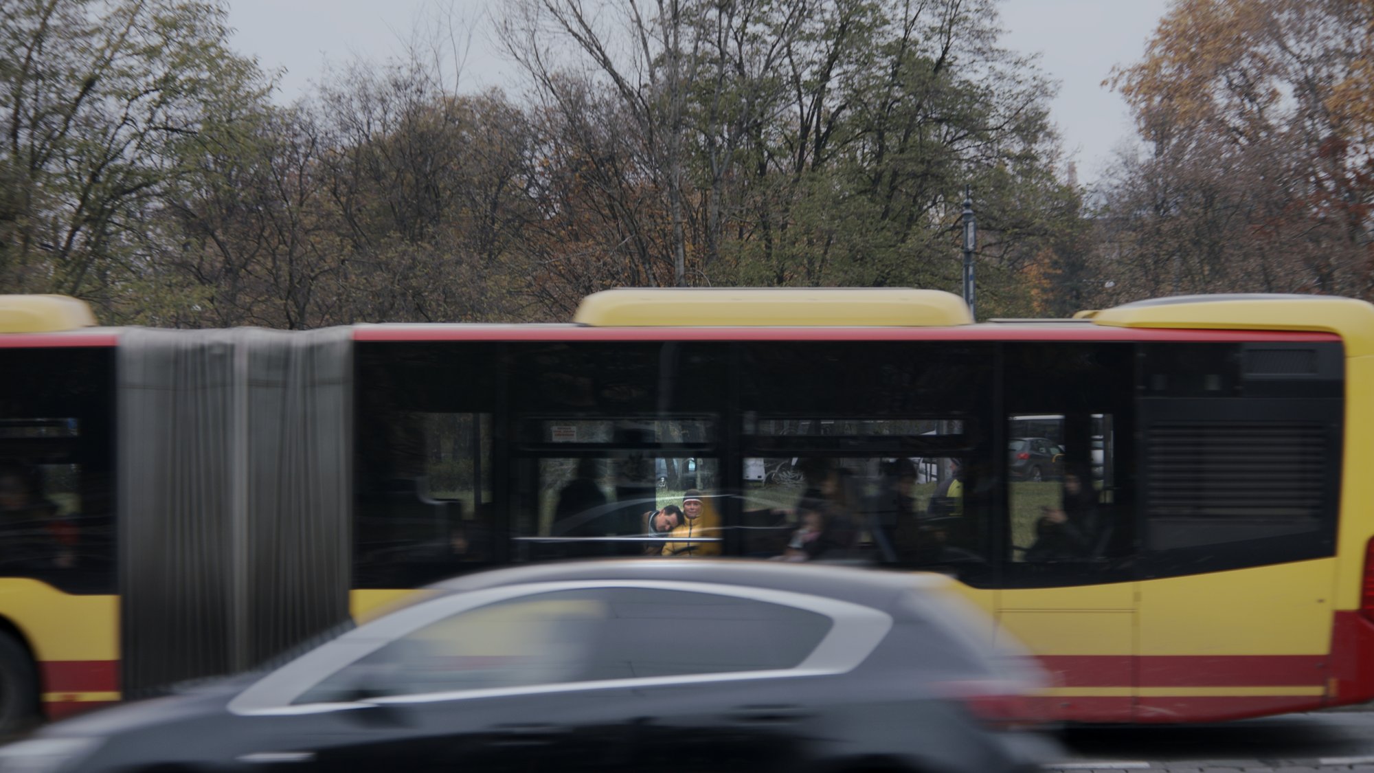 A yellow city bus passing on a tree-lined street - Plantpur commercial
