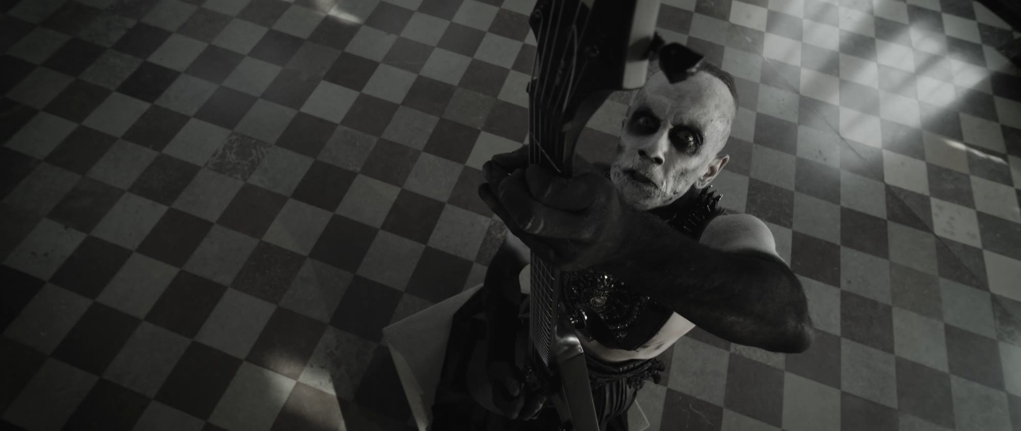 Behemoth music video still - musician pointing a bass guitar toward the camera on the checkered floor