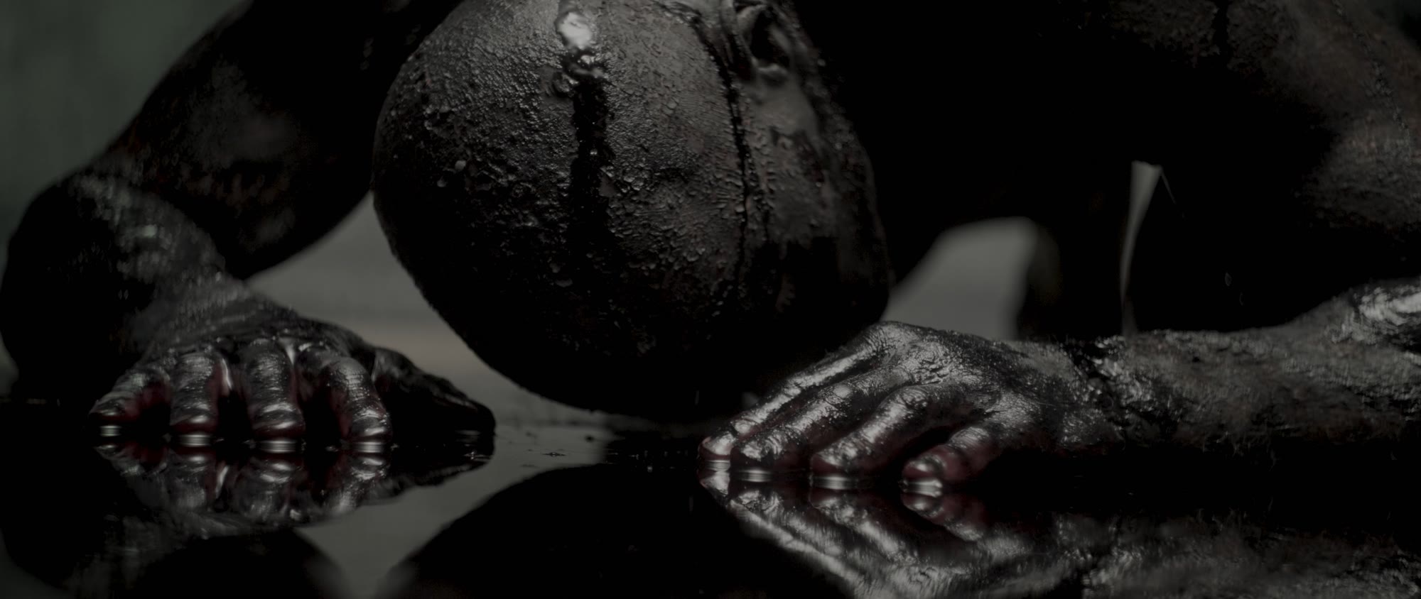 Behemoth music video still - two hands reaching toward a dark reflective surface