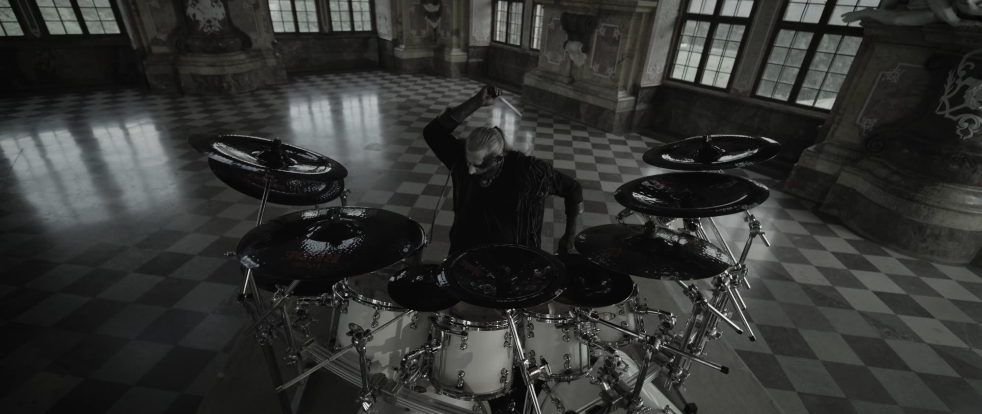 Behemoth music video still - drummer performing on a white drum kit in the middle of the checkered ballroom floor
