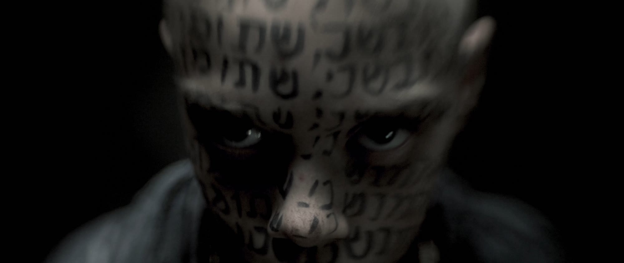 Behemoth music video still - close-up of eyes on a face covered in tattooed script