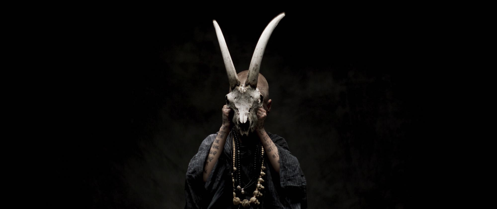 Behemoth music video still - figure holding a goat skull mask up in front of their face