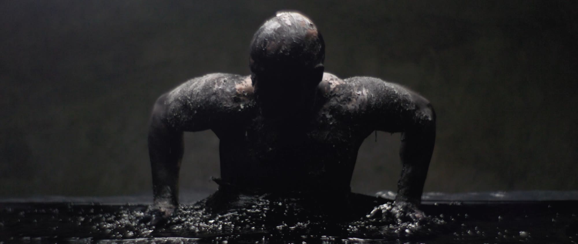 Behemoth music video still - figure emerging from a dark liquid surface, seen from behind