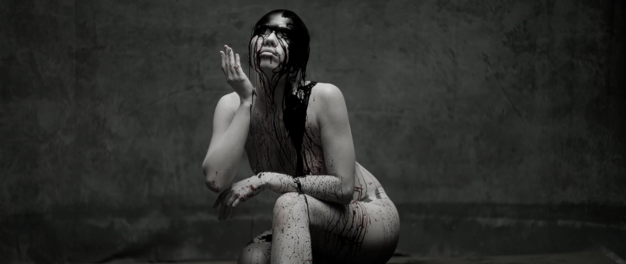 Behemoth music video still - contorted tattooed figure crouching low on the floor
