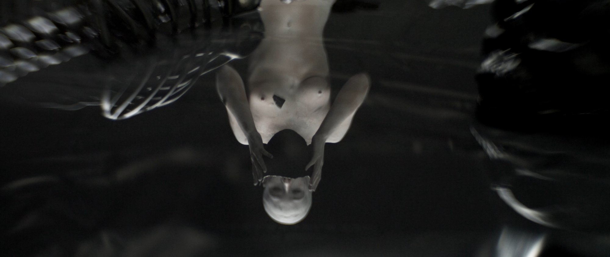 Behemoth music video still - hand reflected on a dark, glass-like liquid surface