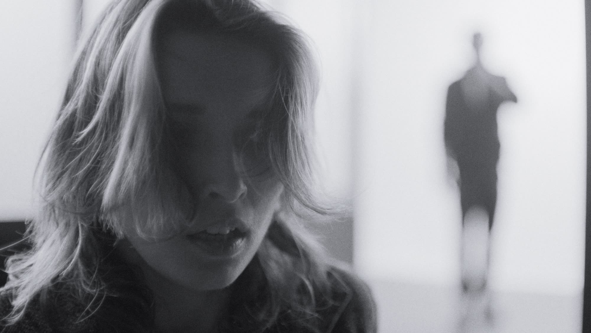 Extreme close-up, a hand near her neck, hair falling across her face, backlit window behind