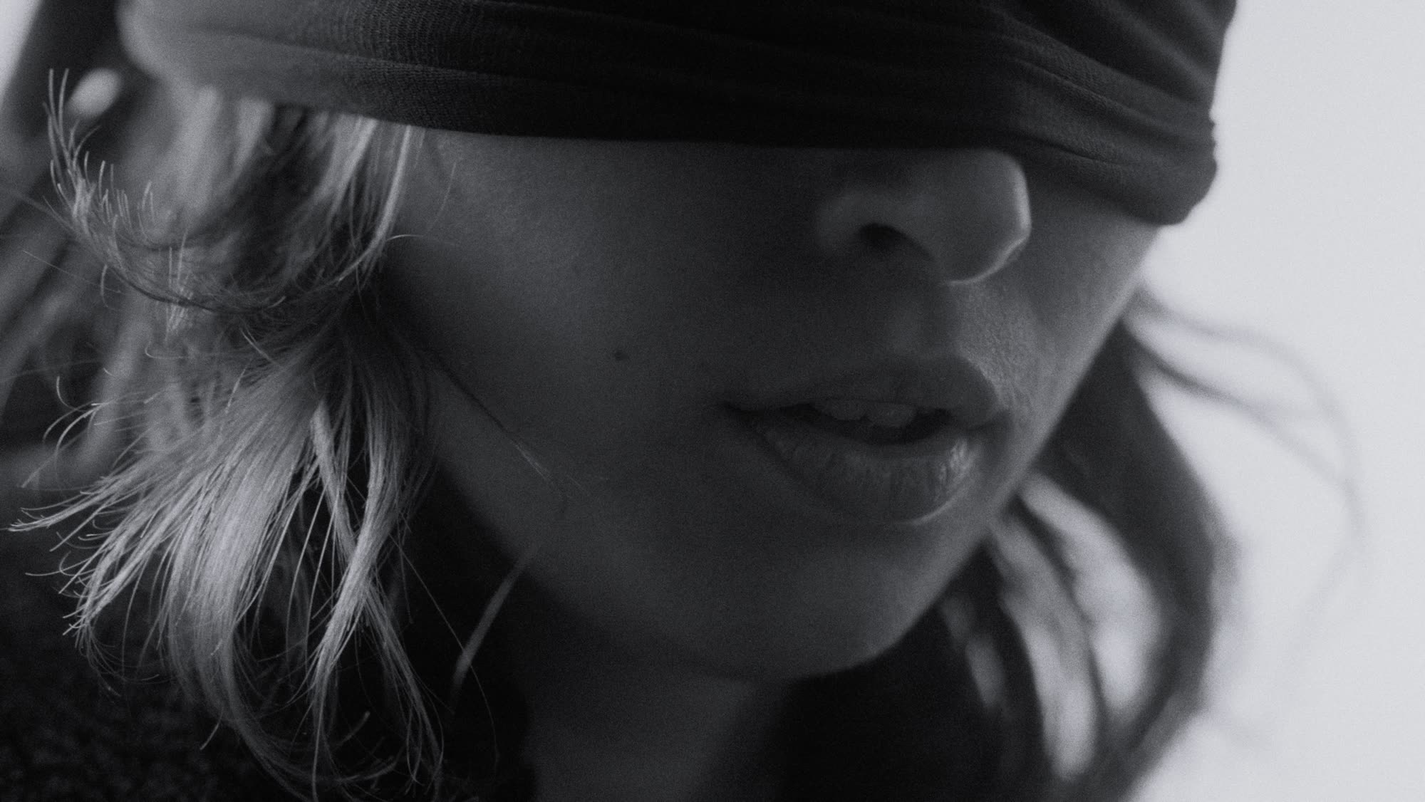 Close-up, blindfold-like fabric across her eyes, soft window light on her face