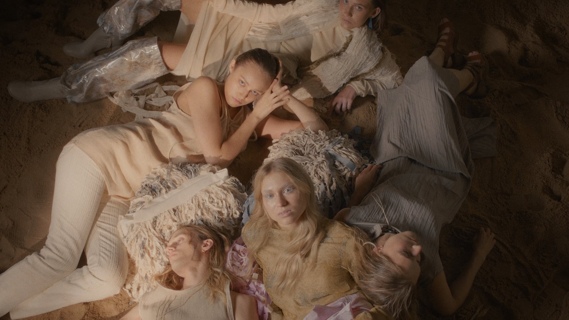 Group of models in cream gowns embracing closely against a dark background - Wrocław Fashion Week Collections