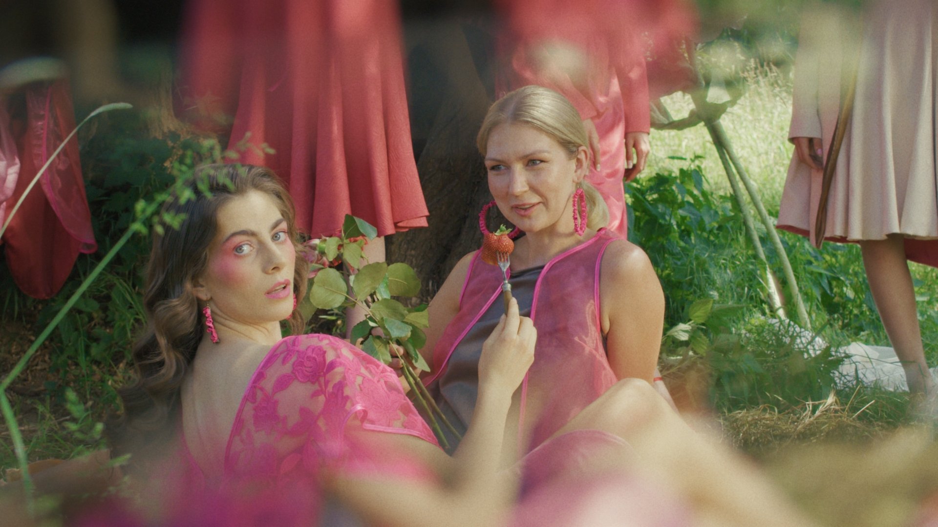 Two models in pink gowns seated together in a garden - Wrocław Fashion Week Collections