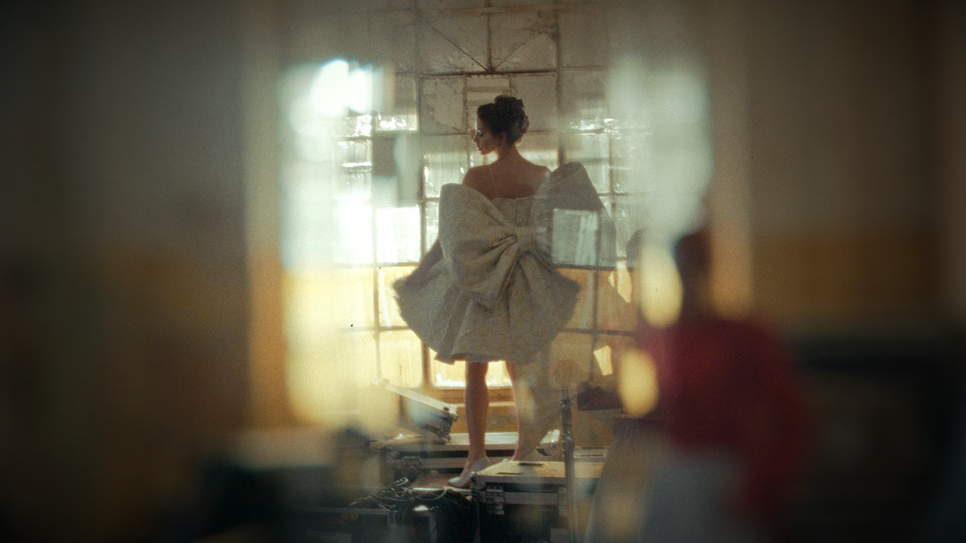Wide shot of a set with a figure seated under warm light, blurred figure in the foreground - Wrocław Fashion Week Collections