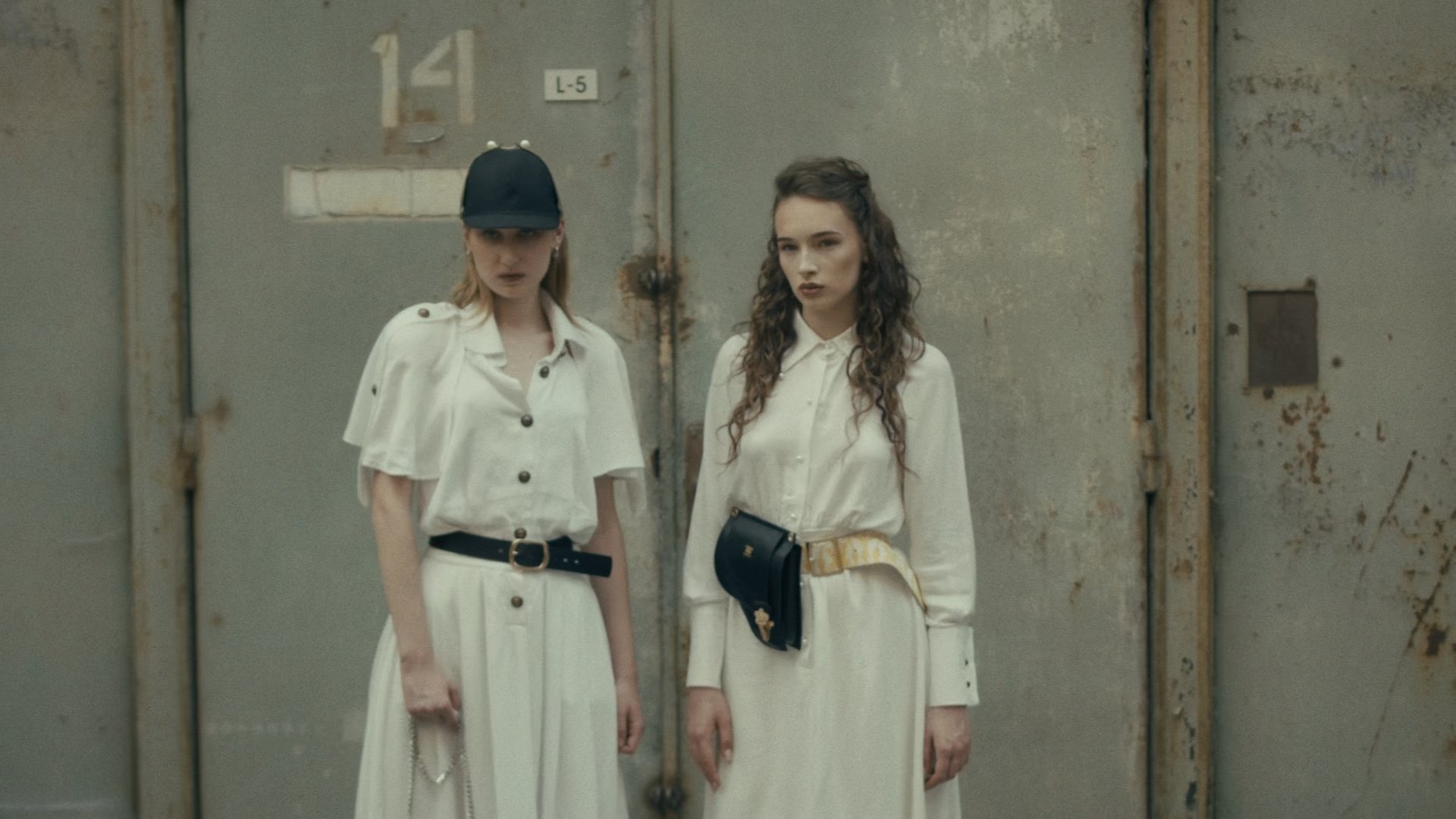 Two models in white dresses and caps standing at an industrial doorway - Wrocław Fashion Week Collections