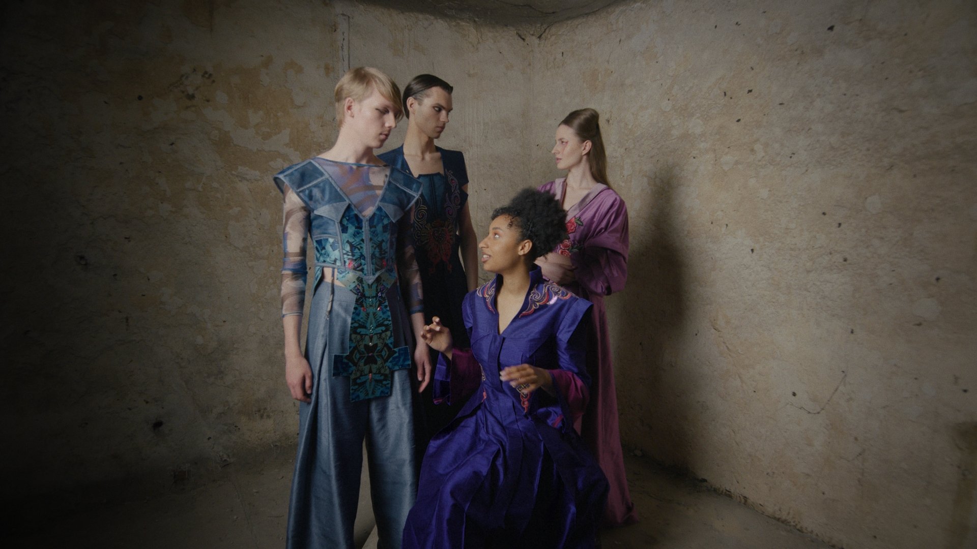 Four models in ornate blue, teal and violet garments gathered in a weathered concrete corner - Wrocław Fashion Week Collections