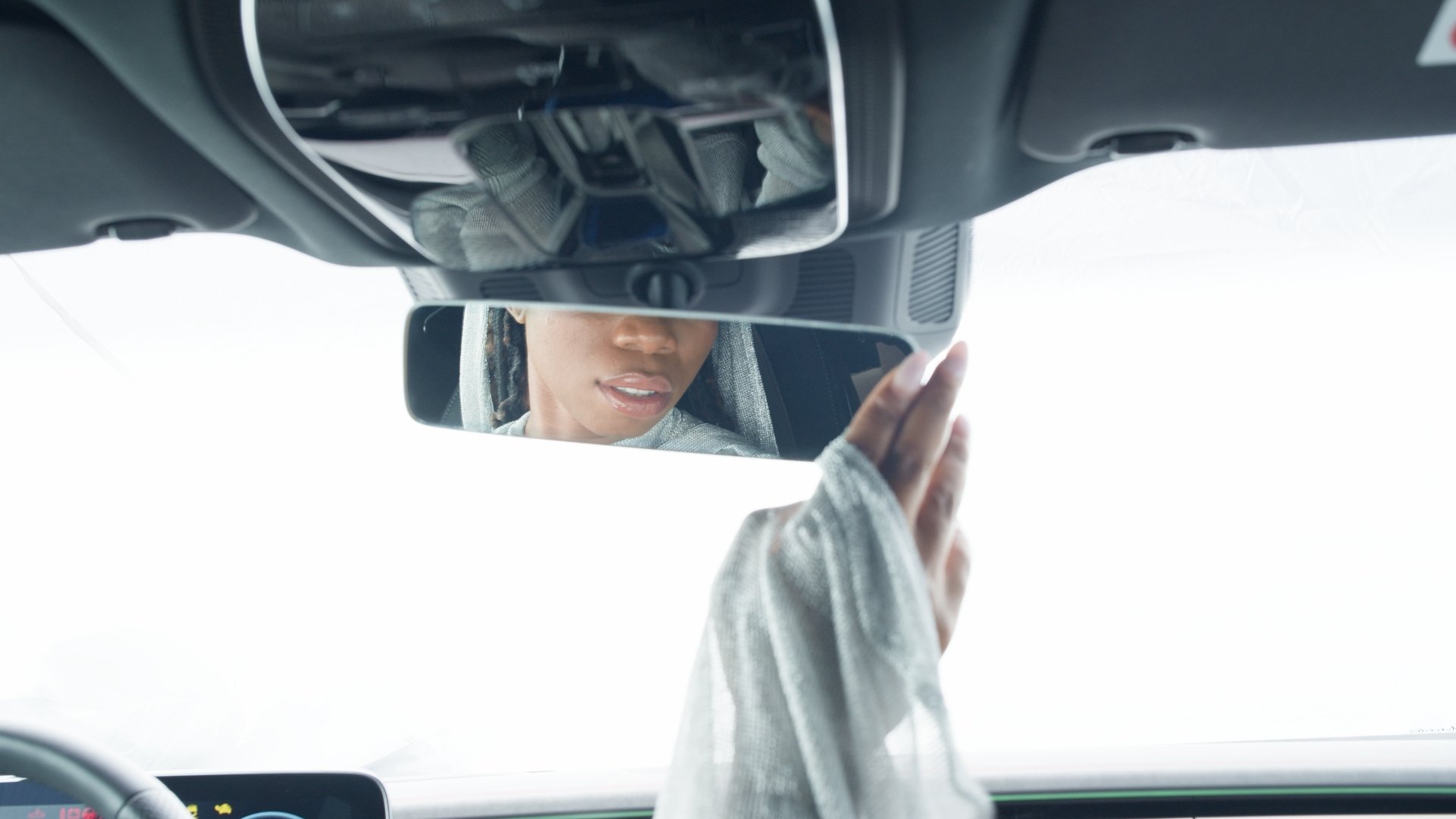 Reflection of a hooded figure in a car's rearview mirror, hand adjusting it - Wrocław Fashion Week Collections