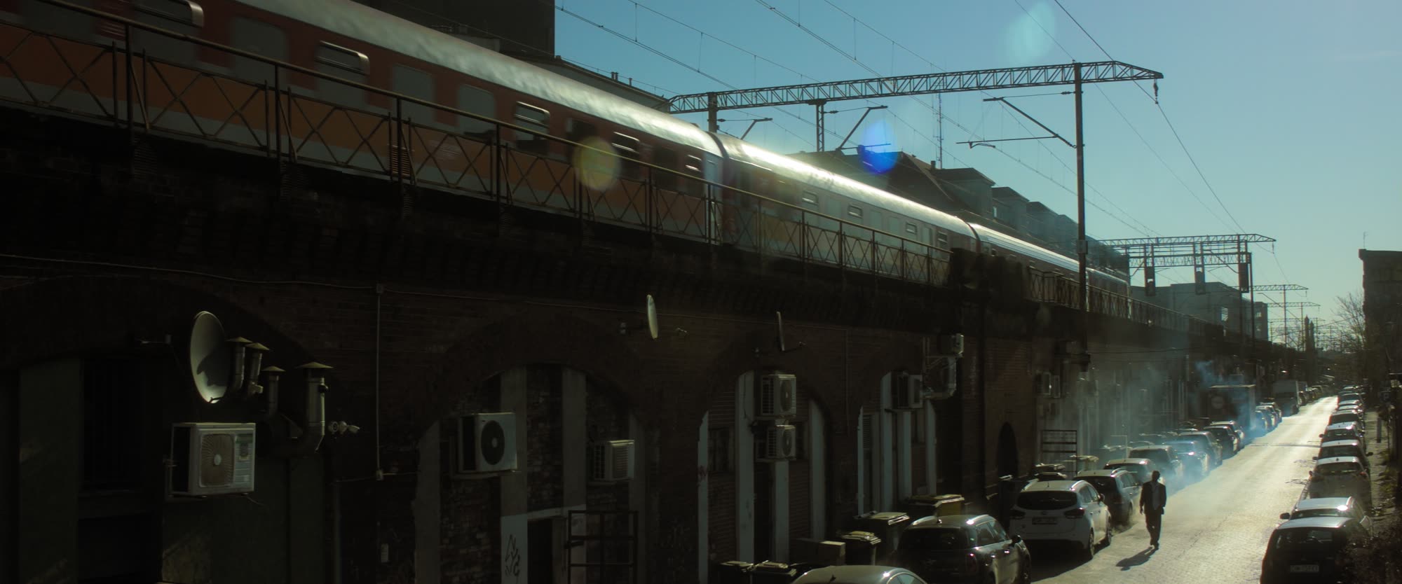 Passenger train crossing a brick viaduct above a sunlit street
