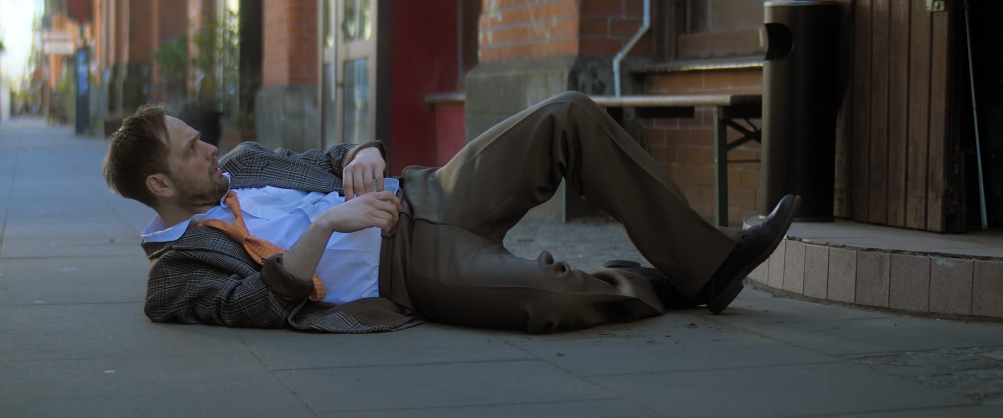 Man in a rumpled suit lying on the sidewalk outside a bar
